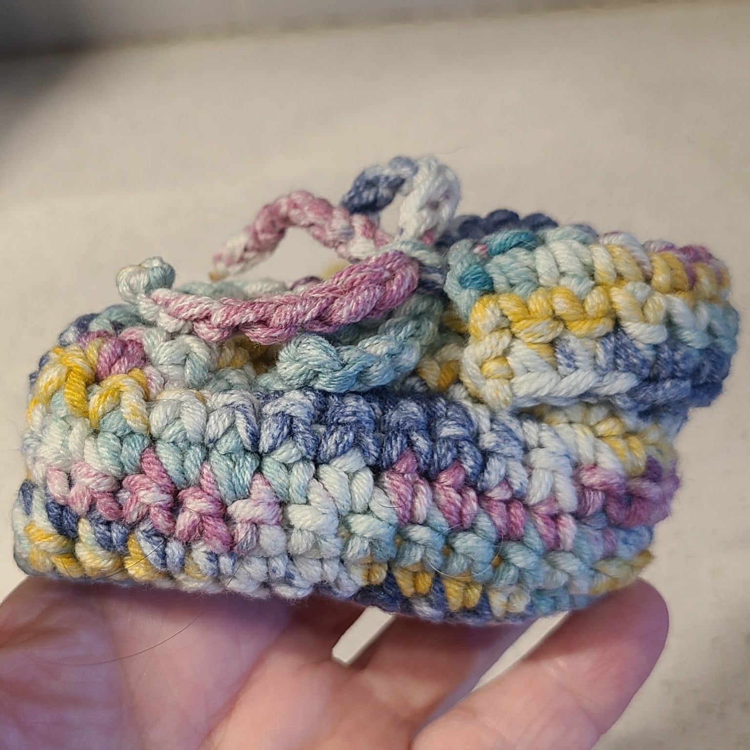 Colorful crocheted baby bootie side view held in a hand against a neutral background