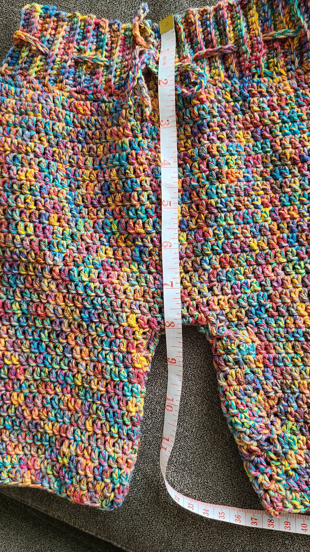 Colorful crocheted pants with a measuring tape on a gray surface