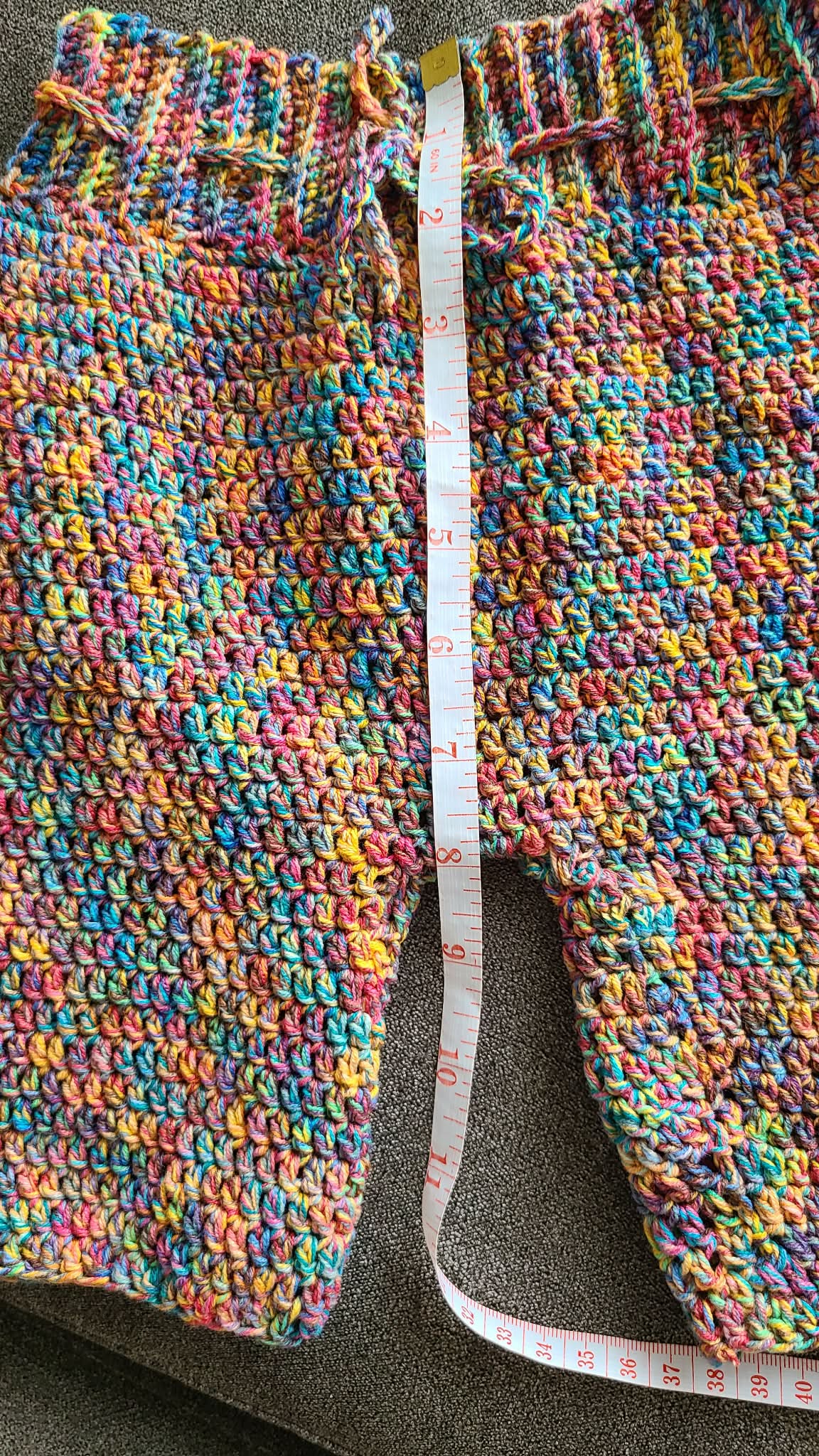 Colorful crocheted pants with a measuring tape on a gray surface