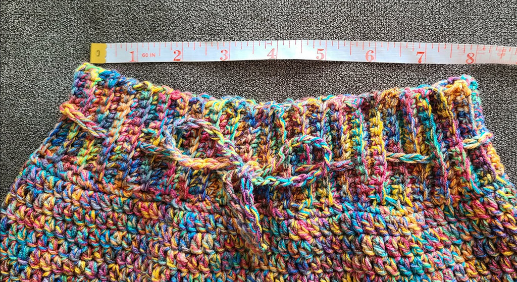 Multicolored crocheted fabric with a measuring tape laid across it on a gray surface