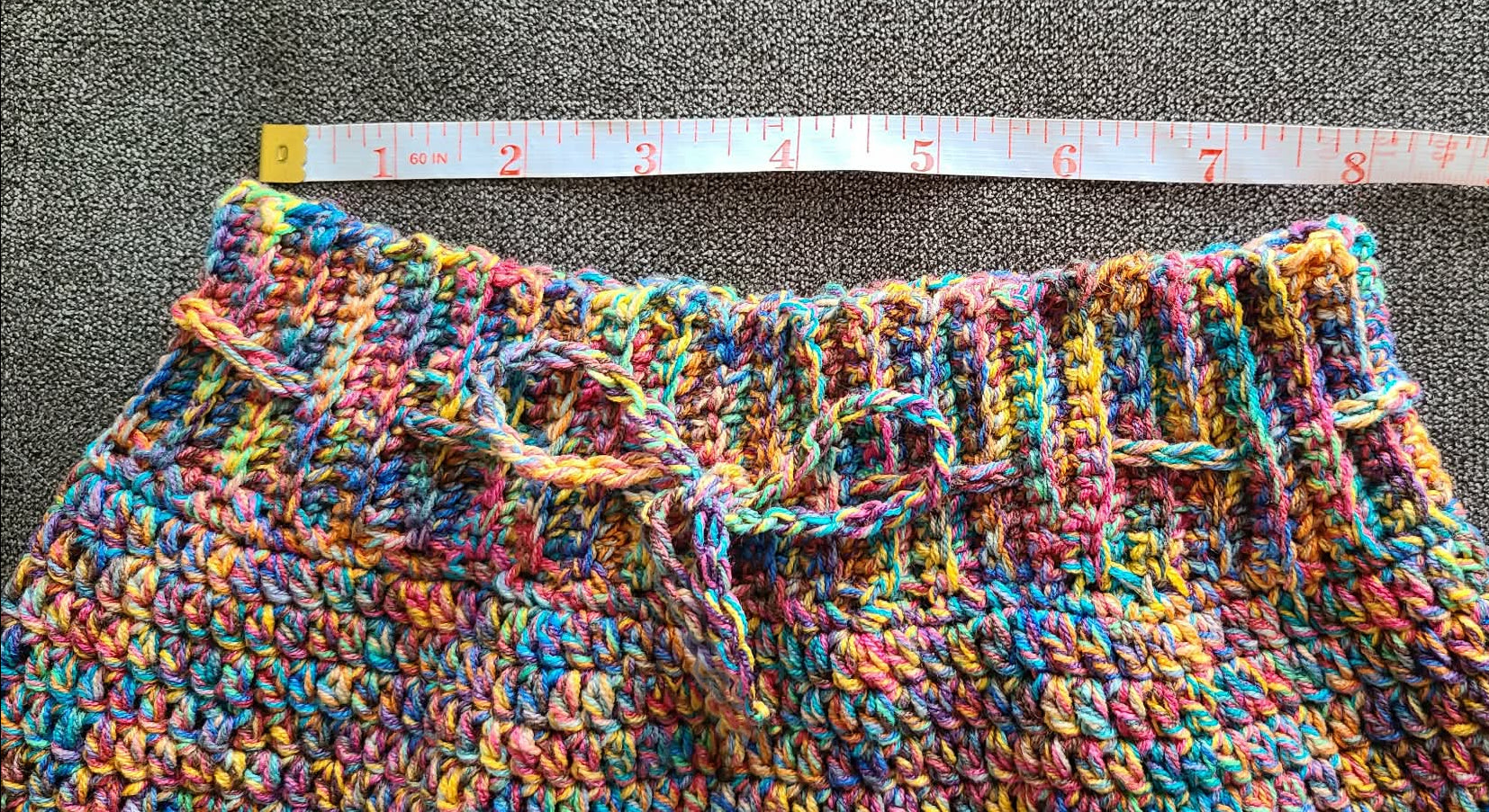 Multicolored crocheted fabric with a measuring tape laid across it on a gray surface