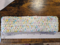 Multicolored crocheted headband on a wooden surface with a ruler for scale.