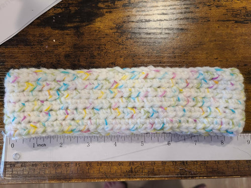 Multicolored crocheted headband on a wooden surface with a ruler for scale.