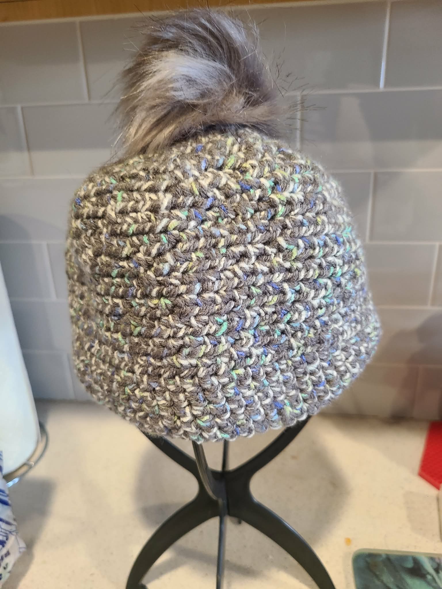 Crocheted beanie with a pom-pom on a mannequin head against a tiled wall background