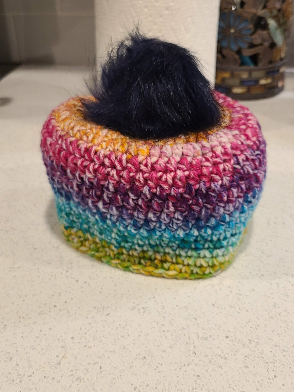 Colorful crocheted baby beanie with a black pom-pom.