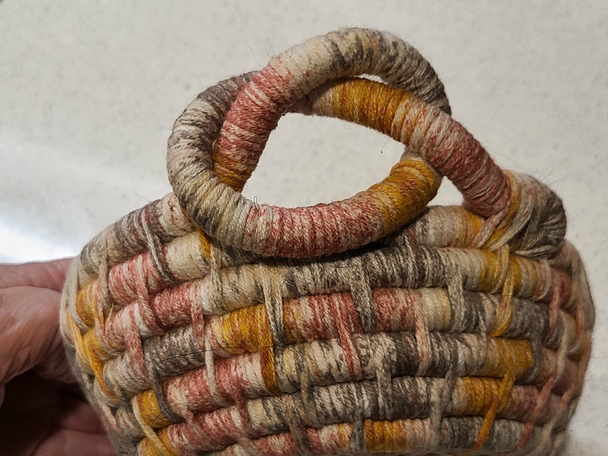 Woven basket with multicolored handle held by a hand against a neutral background