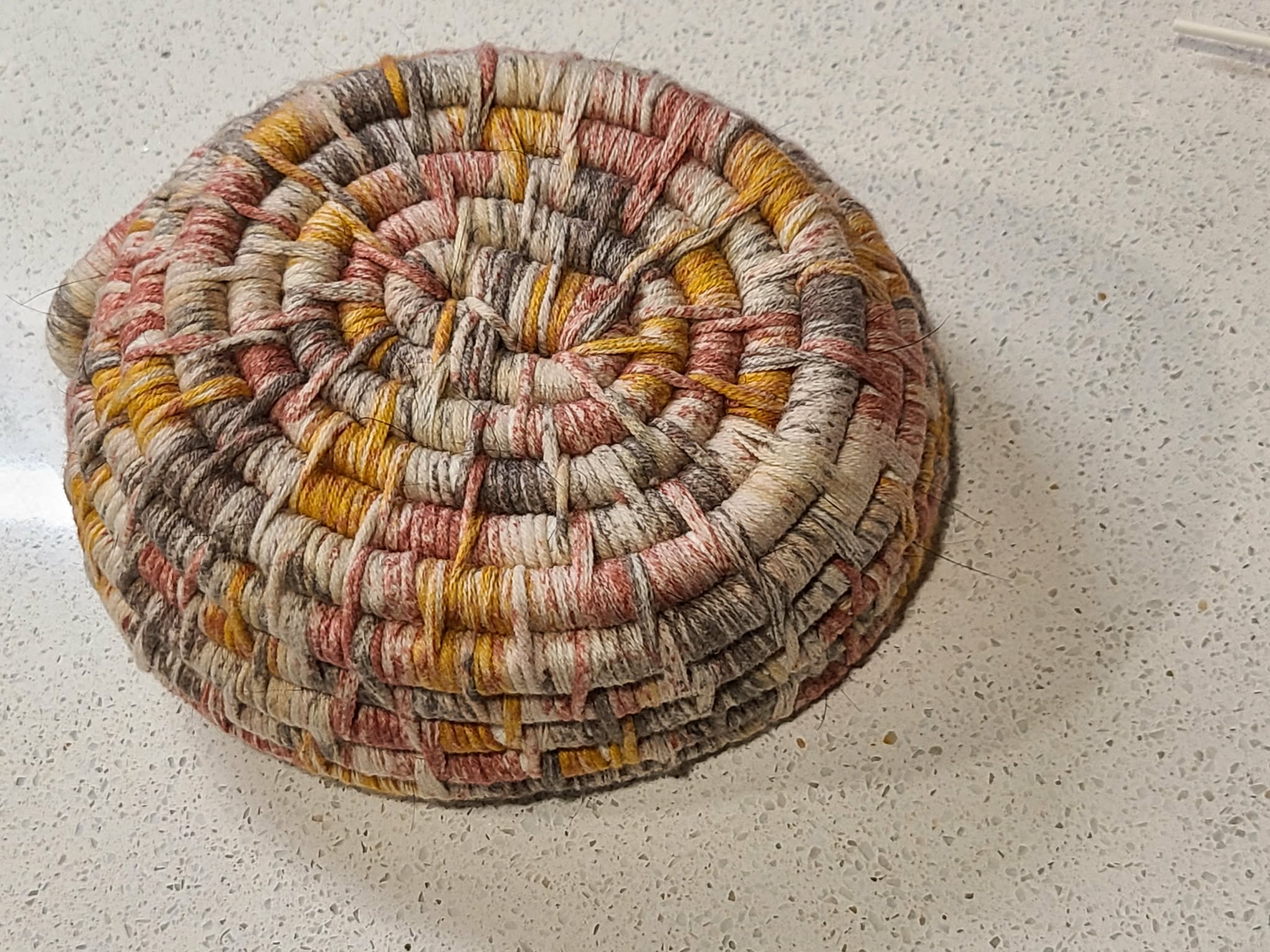 Oval woven coiled basket bottom view with multicolored pattern 